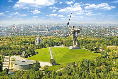 This is a photo showing the gigantic statue standing on a hill, 
surrounded by trees and the memorial chamber with its eternal flame and guards. There is also a Russian Orthodox church 
at the memorial complex.